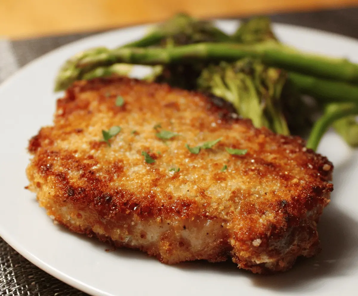Delicious Parmesan Crusted Pork Chops served on a plate with fresh herbs.