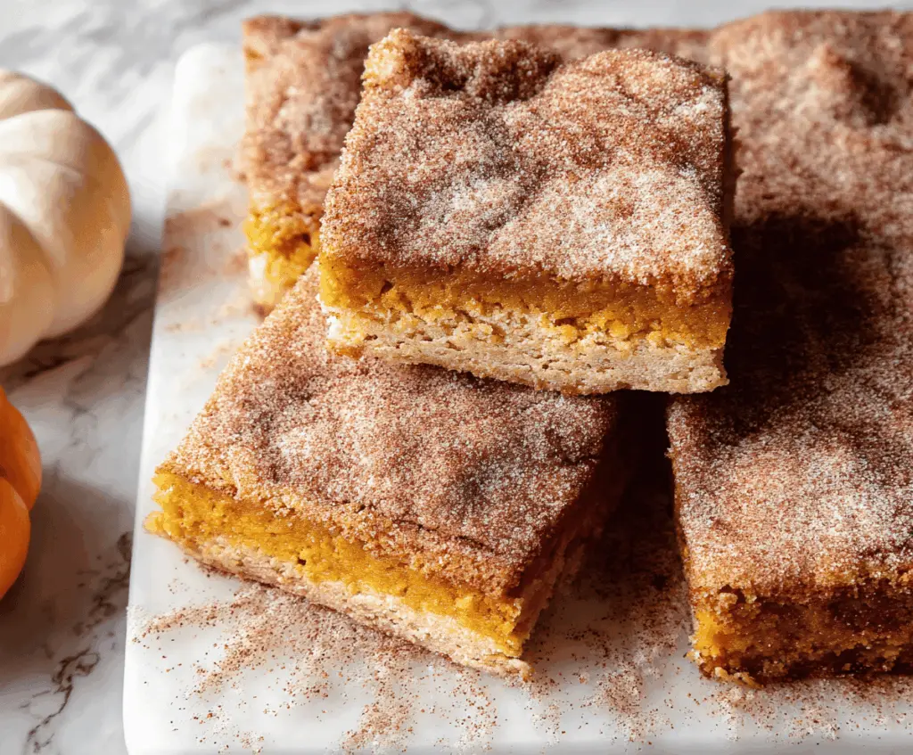 Delicious Pumpkin Snickerdoodle Bars topped with cinnamon sugar on a baking sheet, perfect for fall desserts.
