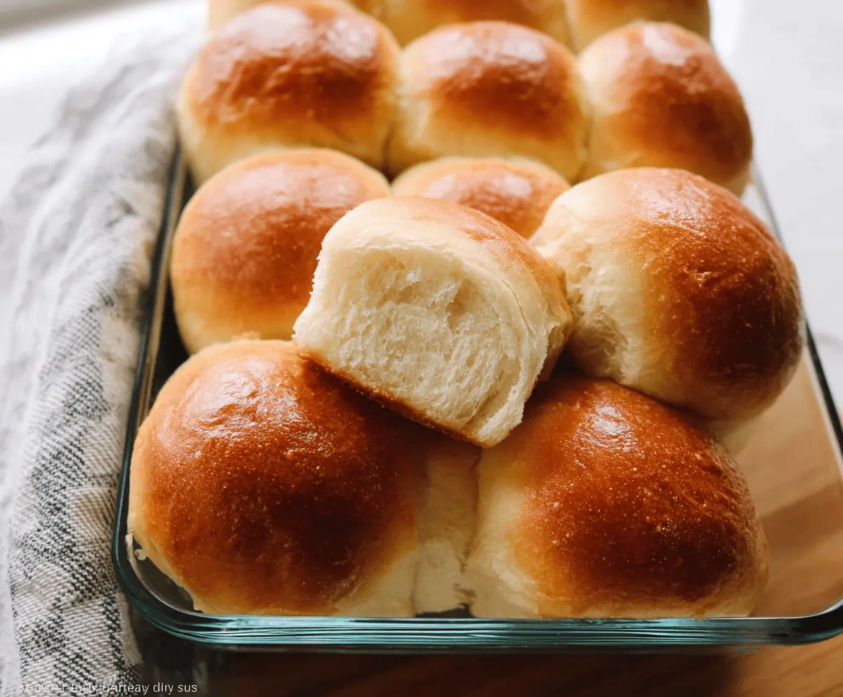 Freshly baked soft dinner rolls with golden crust and fluffy interior on a wooden serving board.