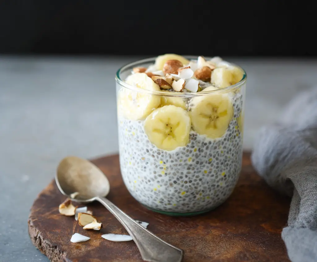 Delicious banana coconut milk chia seed pudding in a glass bowl, topped with fresh sliced bananas and shredded coconut.