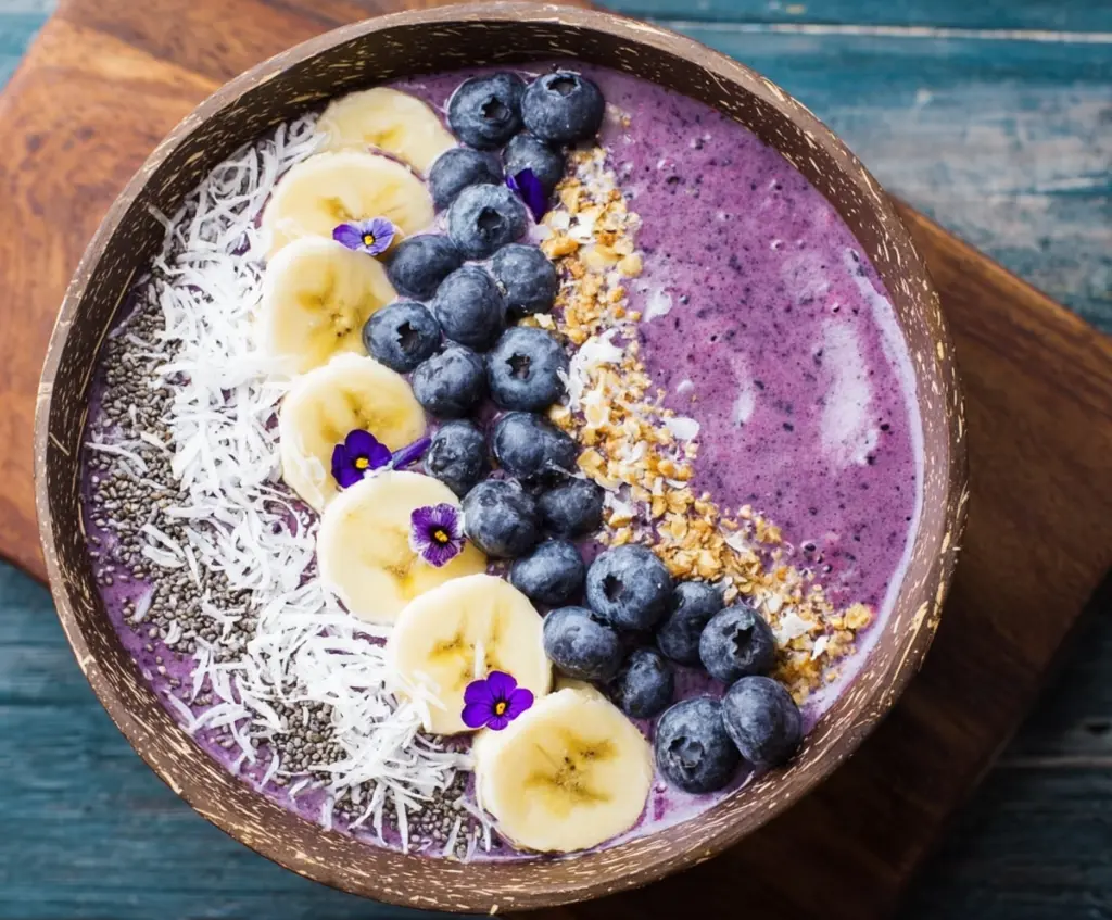 Creamy blueberry smoothie bowl topped with fresh blueberries, granola, and honey on a white plate.