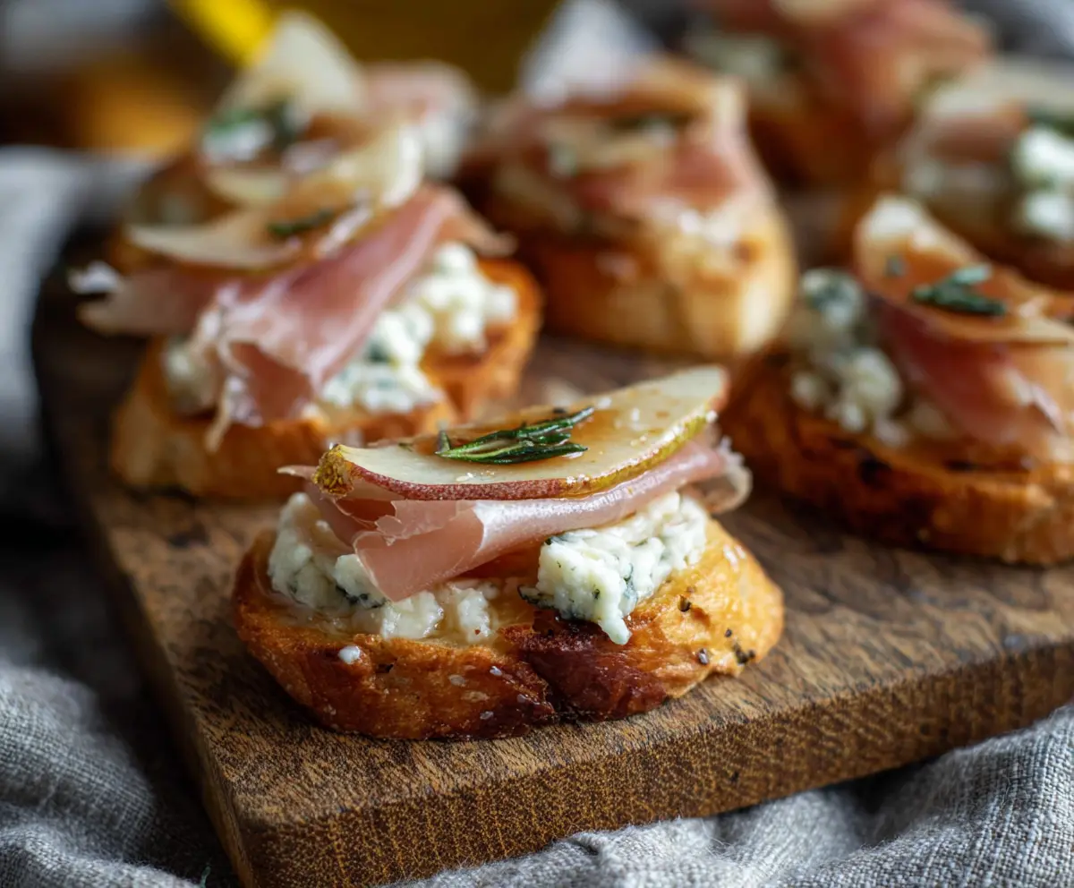 Delicious Prosciutto Pear Gorgonzola Crostini with crispy bread, ripe pears, melted gorgonzola cheese, and prosciutto slices.