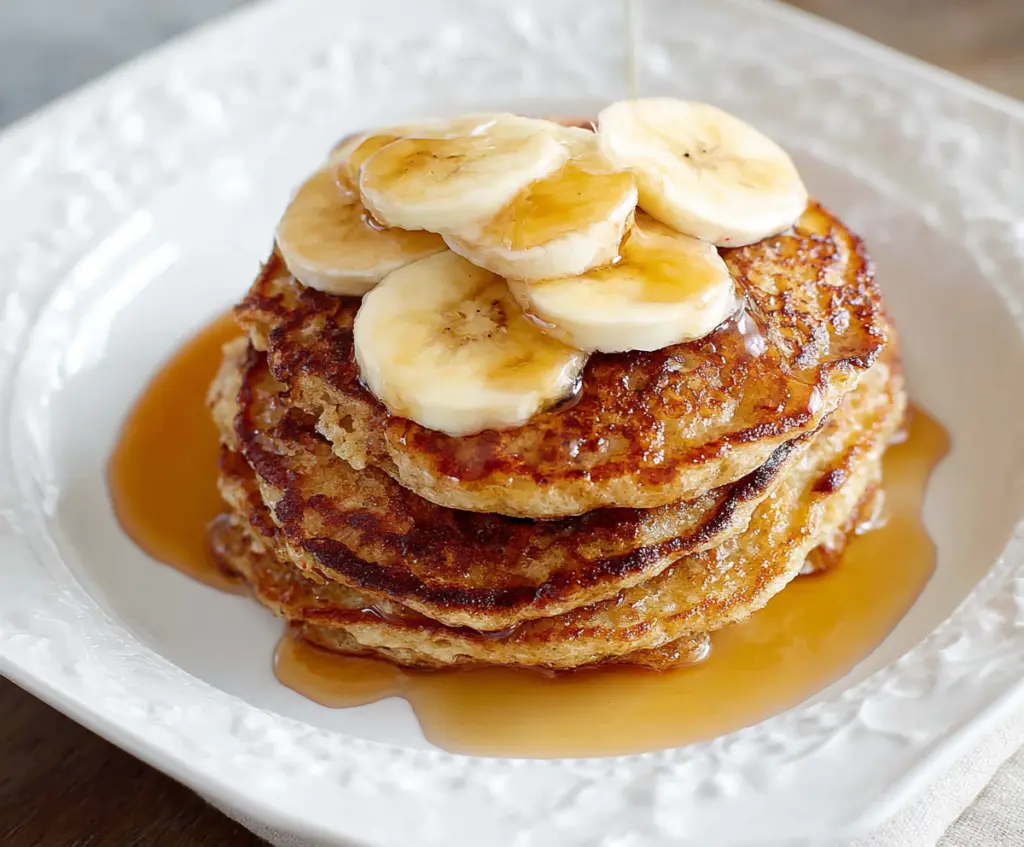 Delicious homemade banana oatmeal pancakes stacked on a plate with fresh banana slices on top.