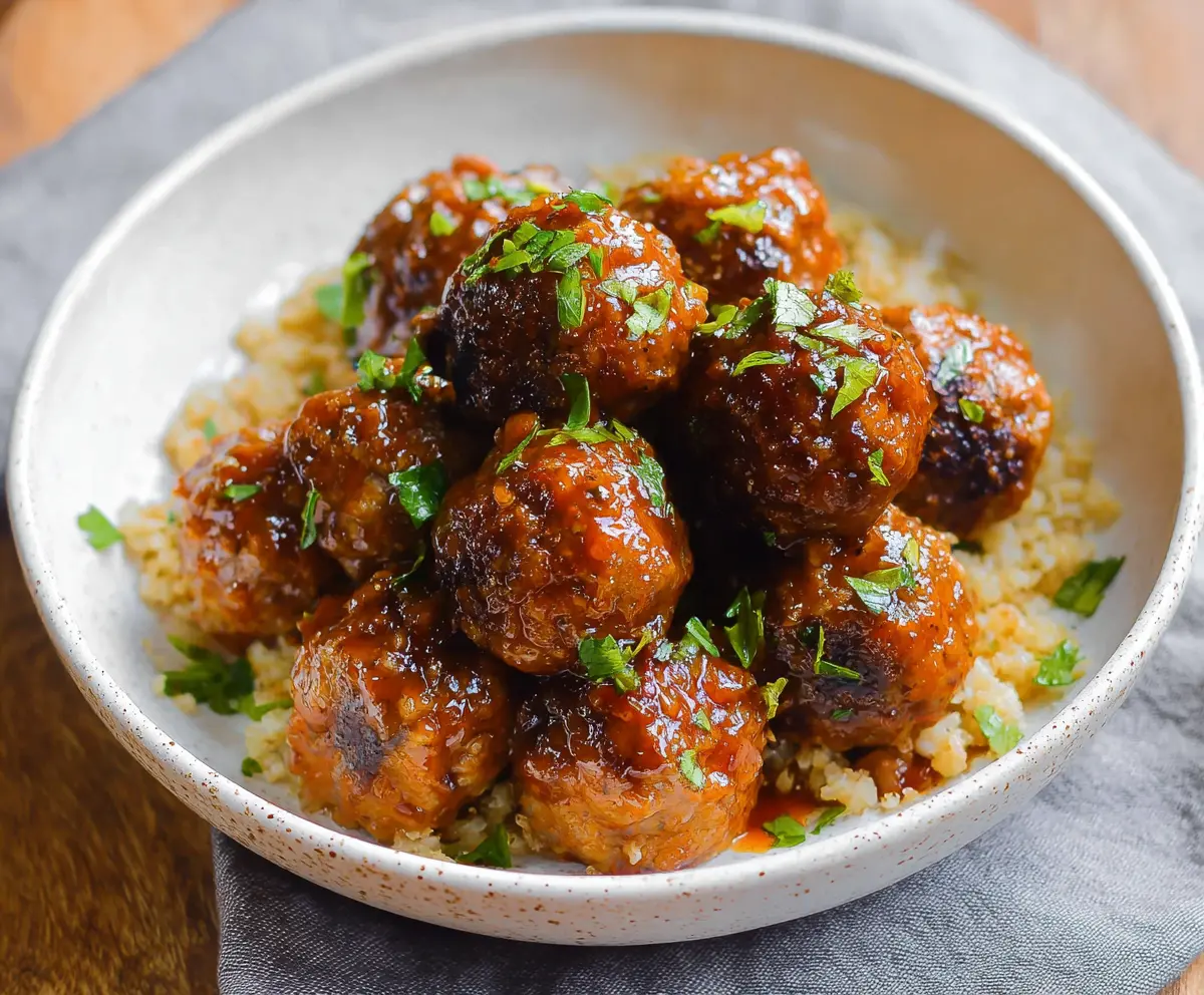 Delicious honey sriracha meatballs garnished with fresh herbs on a white plate