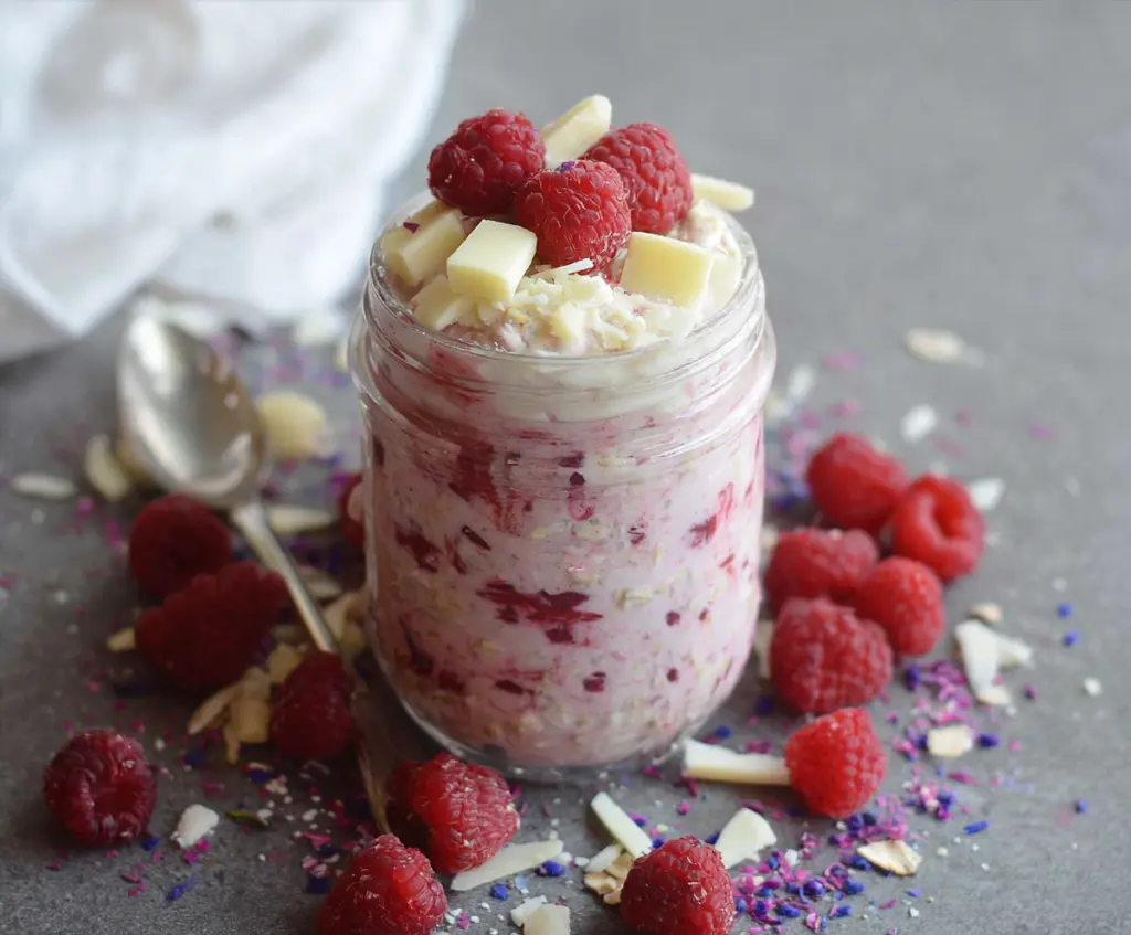 Delicious Raspberry White Chocolate Overnight Oats in a glass jar with fresh raspberries and white chocolate chips