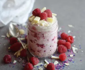 Delicious Raspberry White Chocolate Overnight Oats in a glass jar with fresh raspberries and white chocolate chips