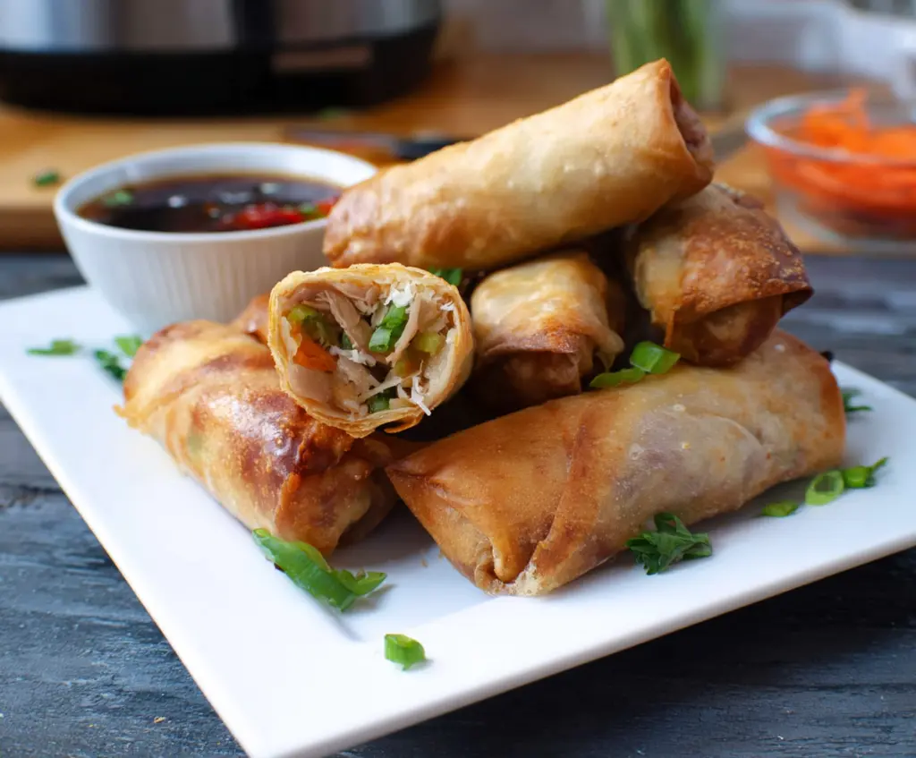 Crispy golden air fryer spring rolls served on a white plate with dipping sauce